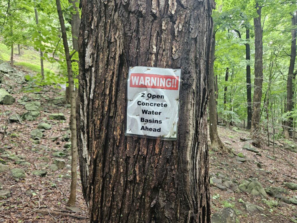 A sign warning hikers of open concrete water basins at Rockleigh Woods Sanctuary and Lamont Preserve